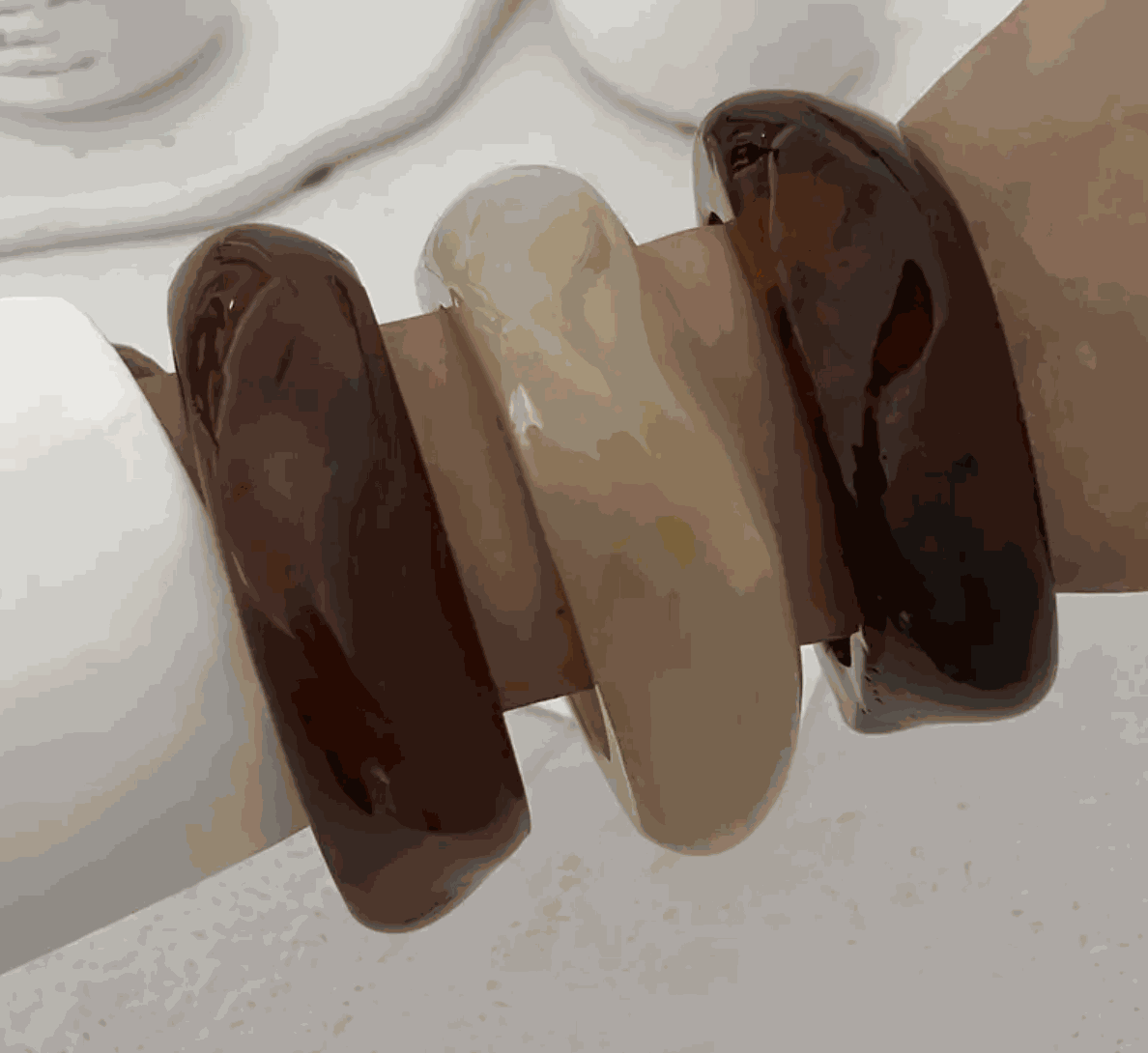 Three Molten Resin Wave Bangles in espresso brown, caramel beige, and deep amber stacked on a wrist